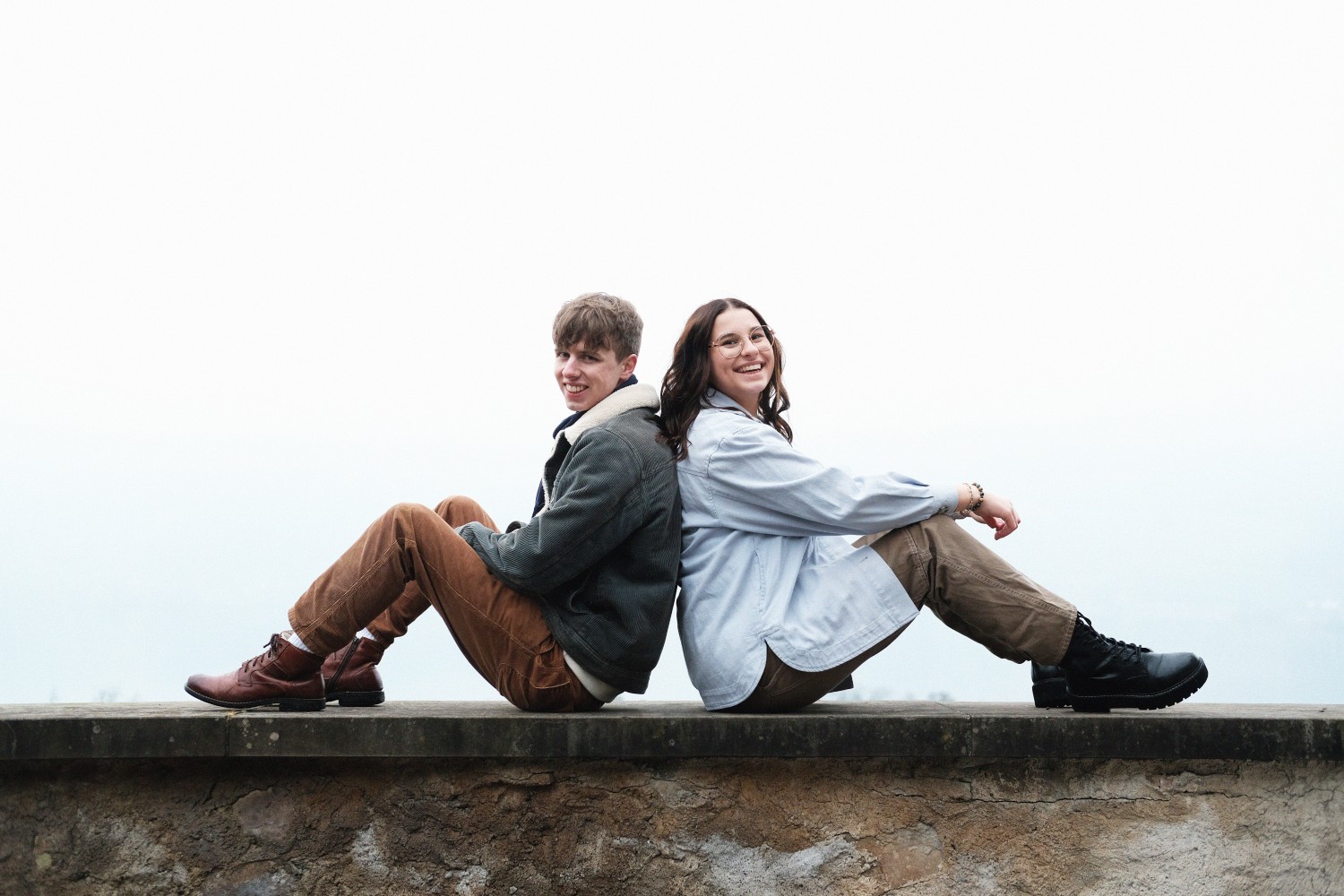 Lea & Johannes auf Mauer sitzend und lachend.